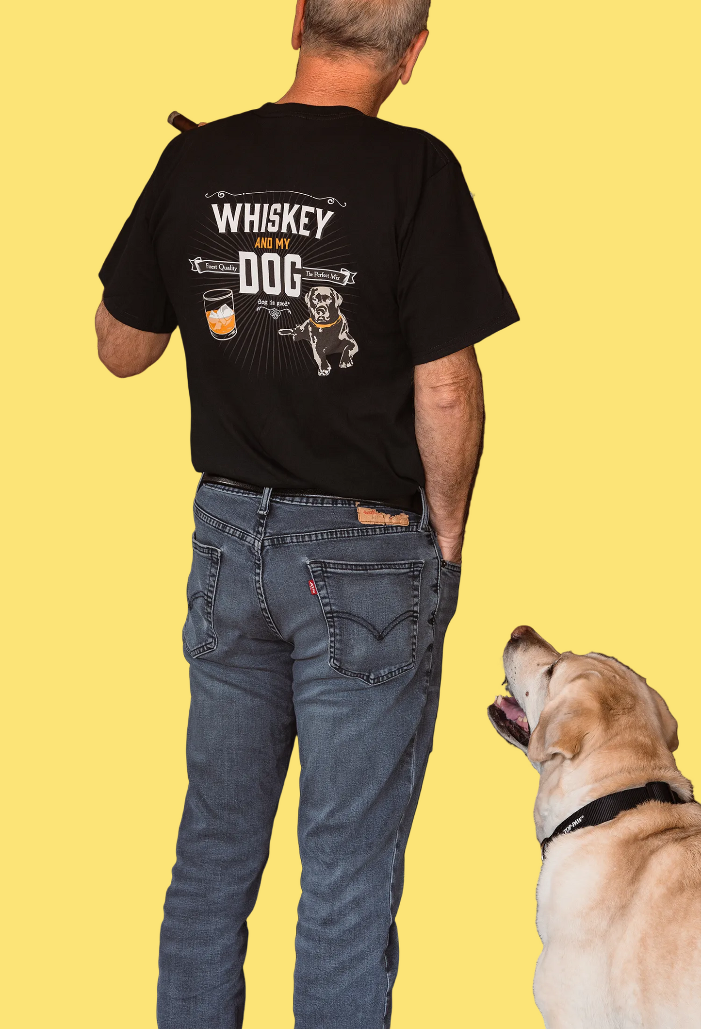 Man wearing a black t-shirt with 'Whiskey and my dog' design, standing next to a dog in a bar setting.