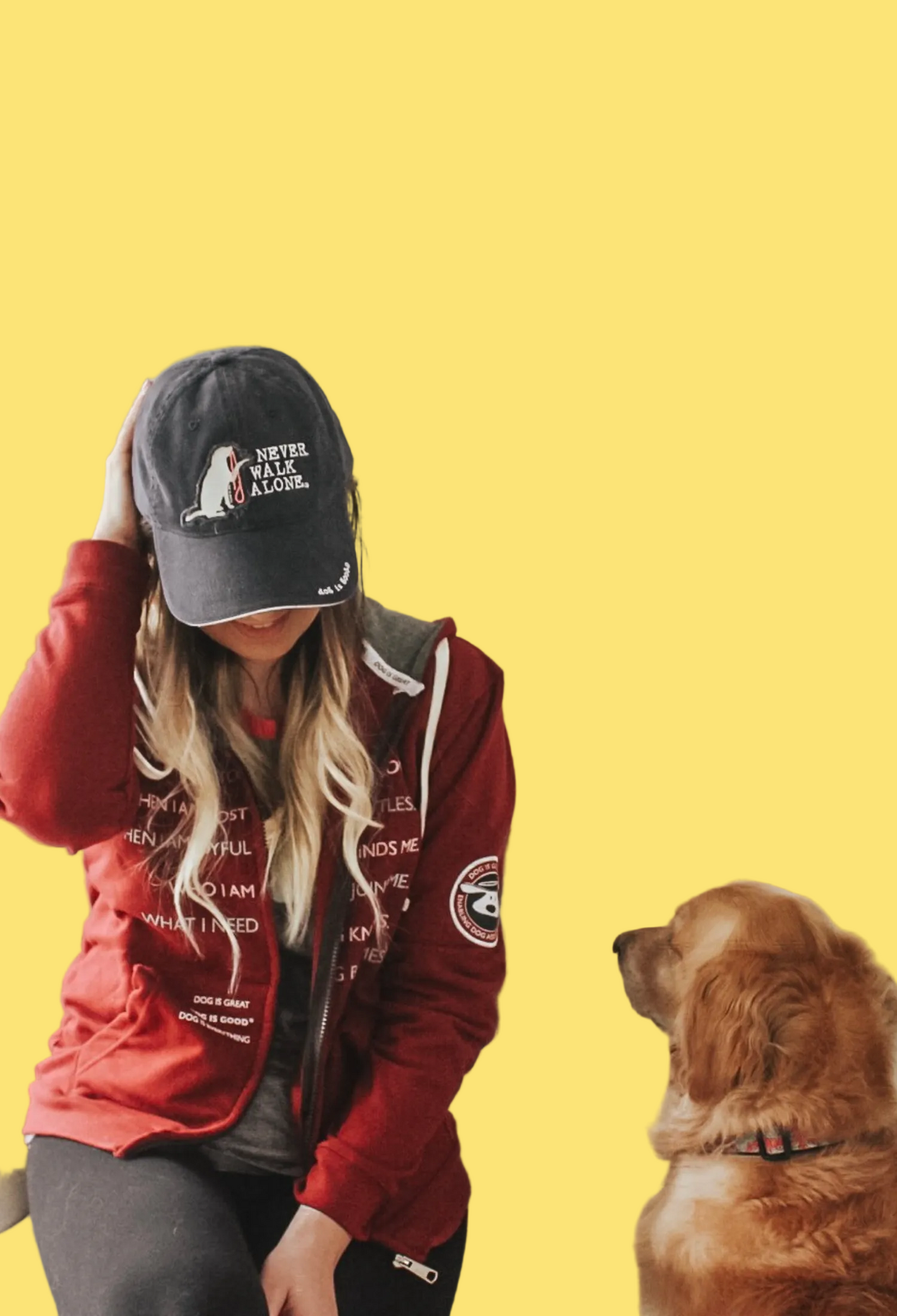 Person wearing a red hoodie and black cap sitting on a couch with a dog.