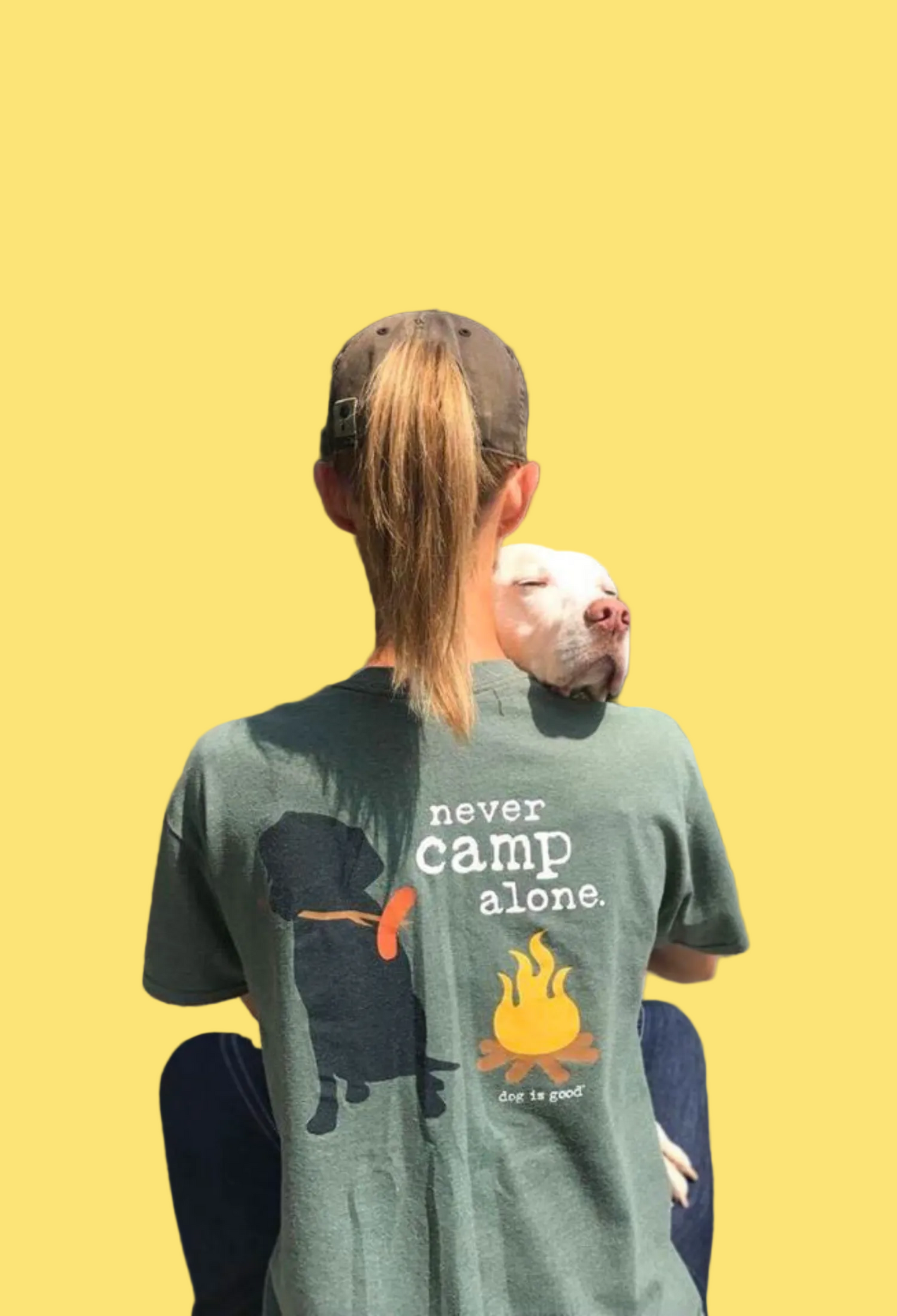 Person wearing a green t-shirt with 'never camp alone' text and graphics, holding a piglet outdoors.