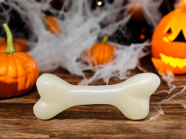 Dog bone-shaped chew toy on a wooden surface with Halloween decorations in the background.