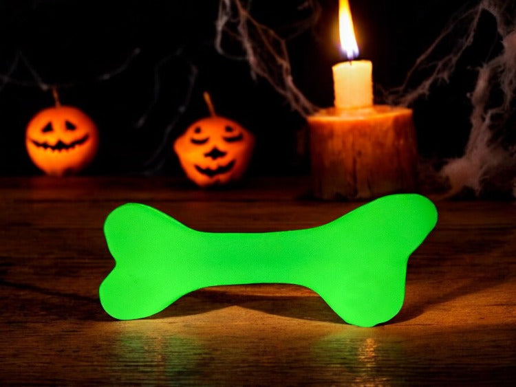 Green bone-shaped object glowing in front of Halloween pumpkins and a candle.